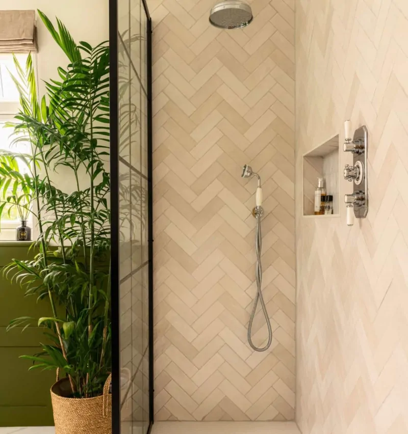 Walk-in shower with pale herringbone tiles, black fittings and plants