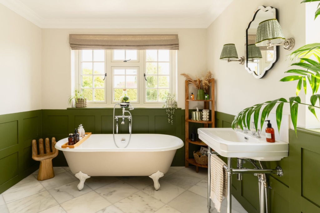 Freestanding bath with dark green wall panelling and traditional bathroom fittings