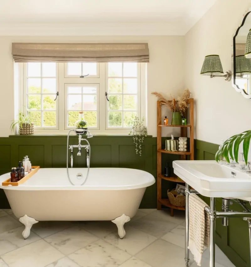 Freestanding bath with dark green wall panelling and traditional bathroom fittings