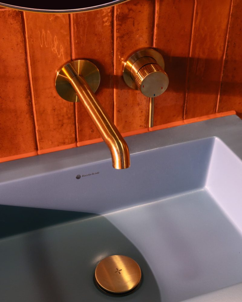 Brushed brass wall-mounted basin tap against rich red bathroom tiles