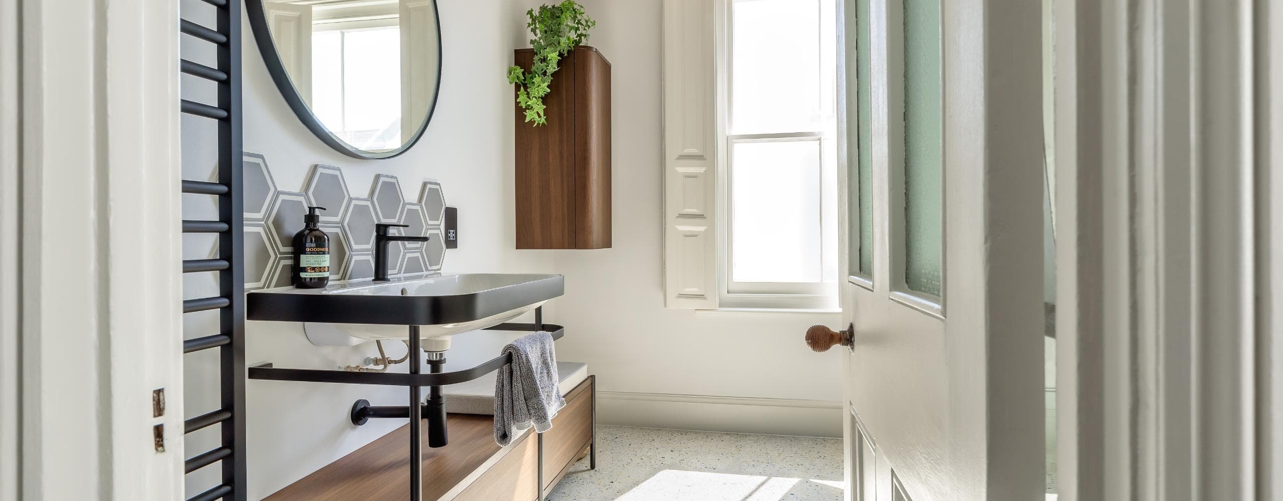 Bright contemporary bathroom with round mirror, dark vanity and timber details