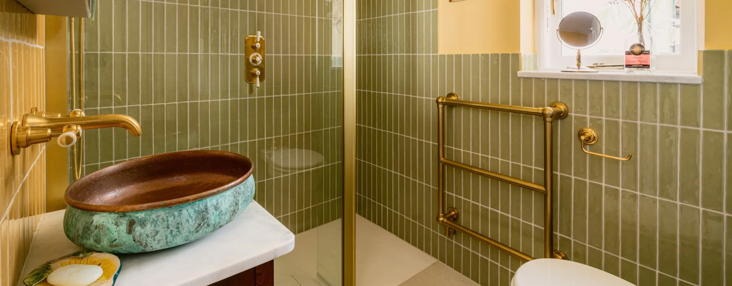 Green tiled bathroom with countertop basin and brass fittings