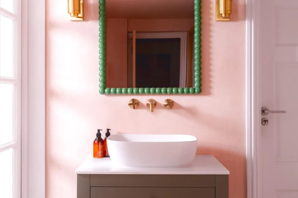 Pink bathroom vanity with green framed mirror and brushed brass fittings