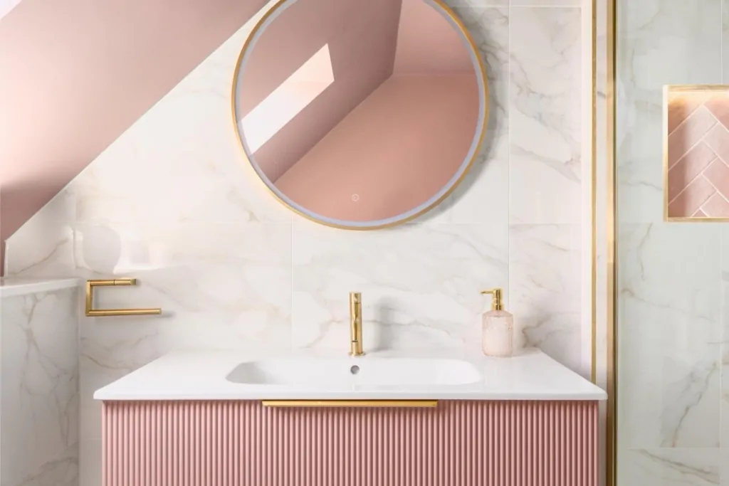 Round bathroom mirror against a soft pink wall beneath a sloping ceiling