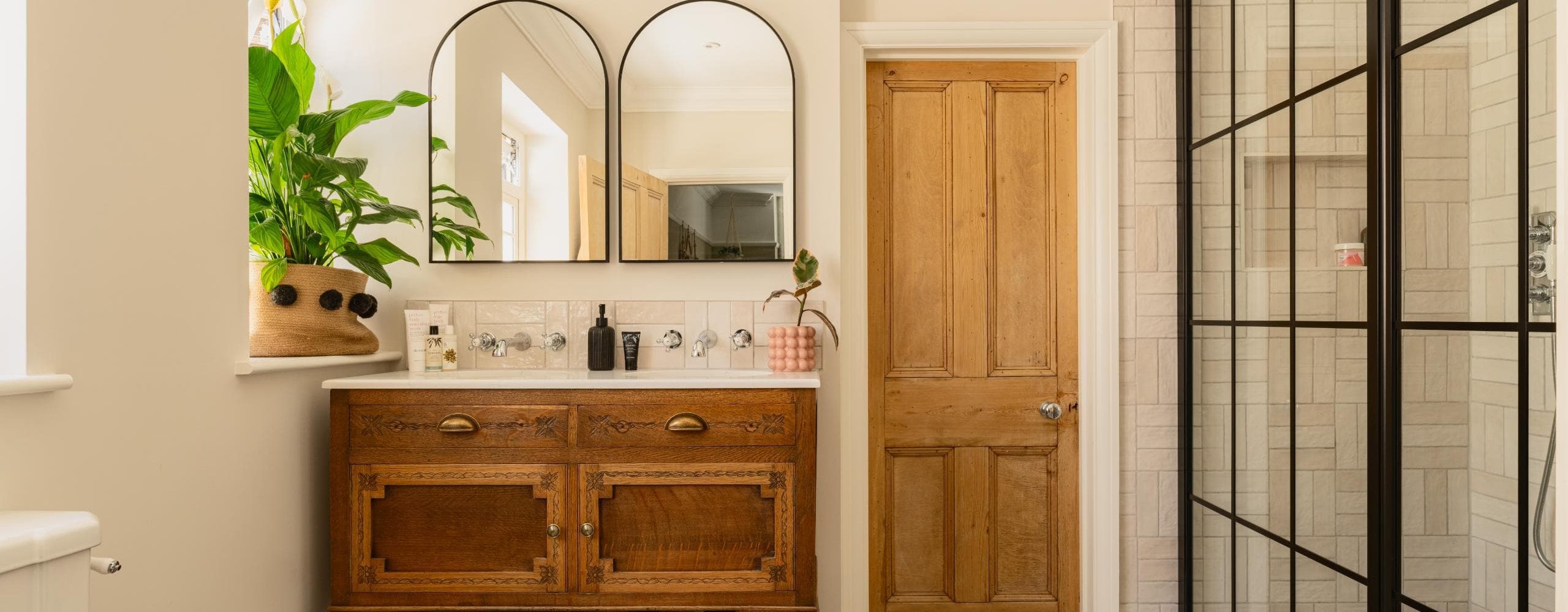Luxury double vanity with arched mirrors, timber cabinetry and indoor plants