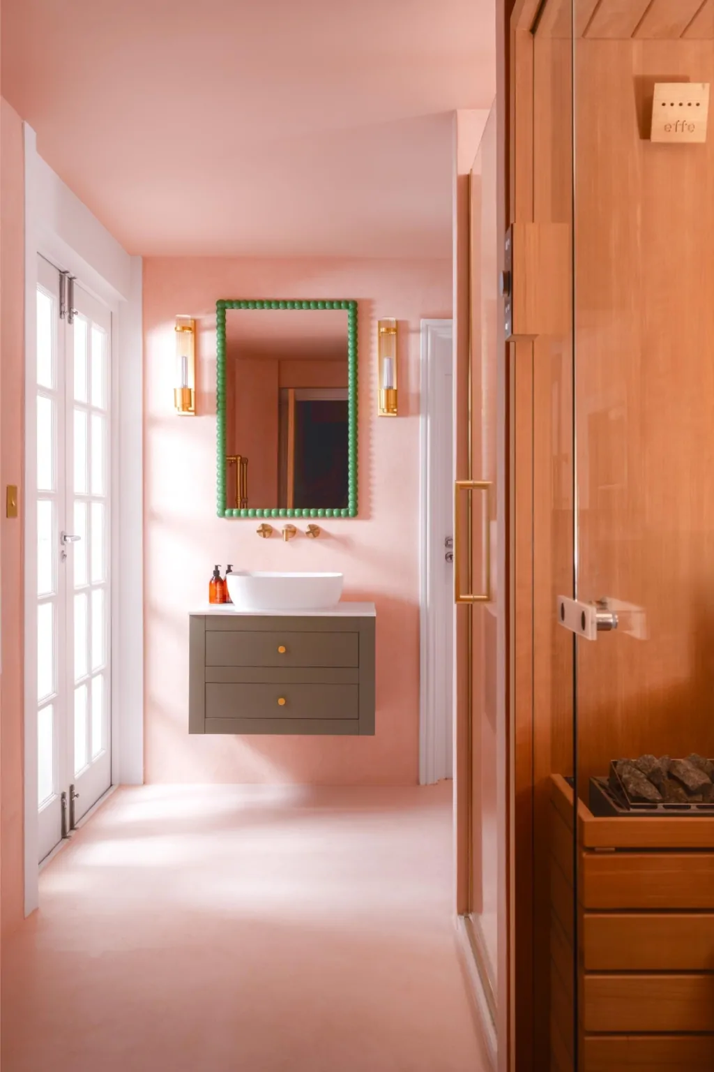 Pink bathroom vanity with timber panelling, green framed mirror and brass details