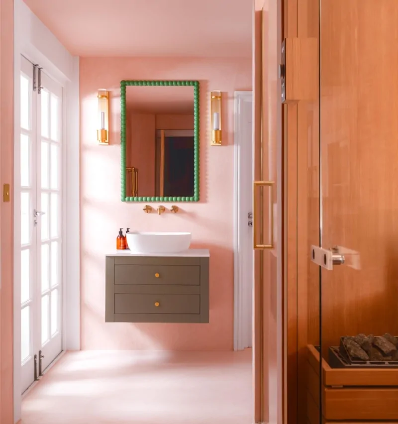 Pink bathroom vanity with timber panelling, green framed mirror and brass details