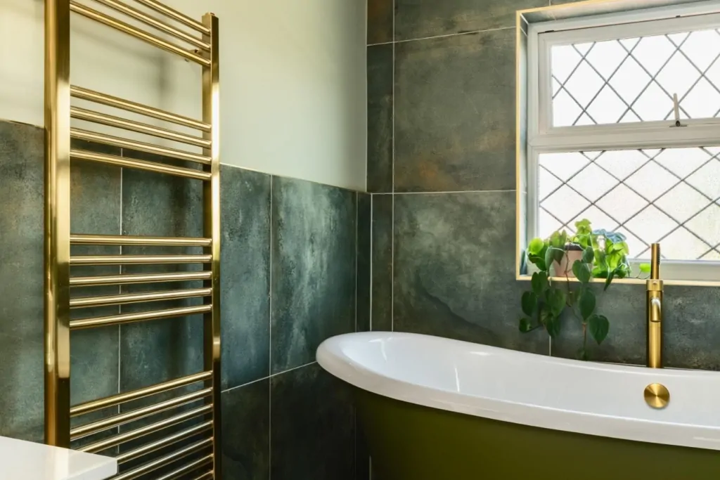 Green marble effect bathroom with freestanding bath, window and brass towel rail