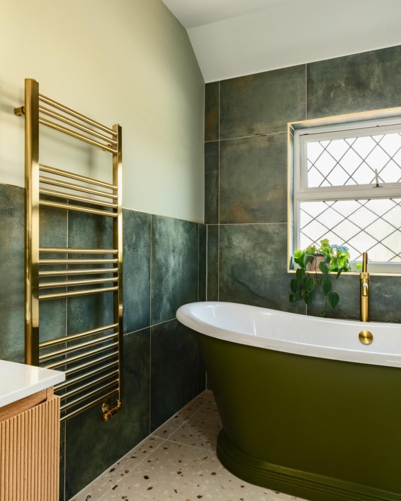 Green marble effect bathroom with freestanding bath, window and brass towel rail