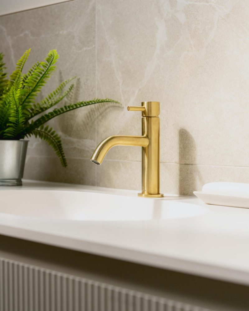 Luxury brass basin tap with greenery and soft neutral bathroom finishes