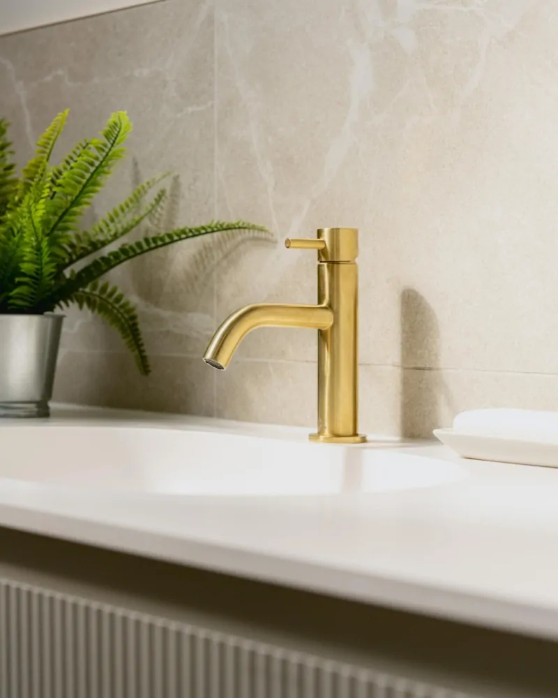 Luxury brass basin tap with greenery and soft neutral bathroom finishes