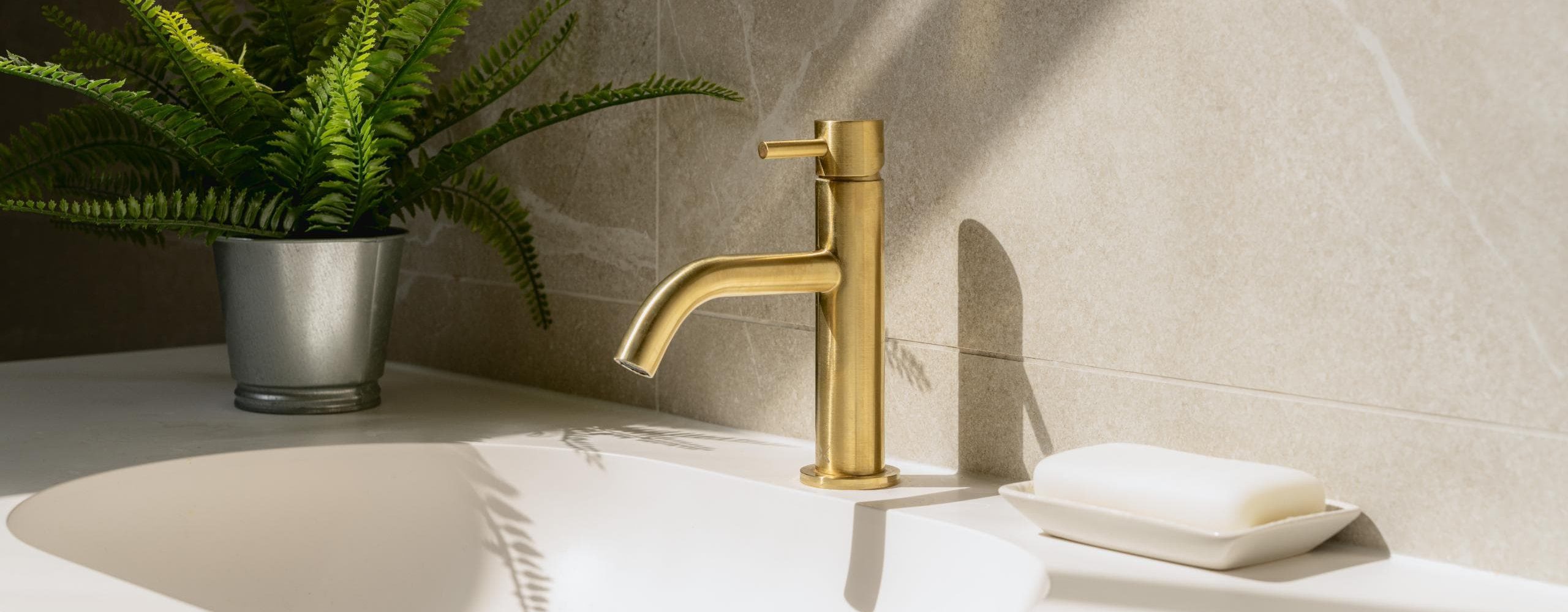 Brushed brass bathroom tap against a neutral stone wall