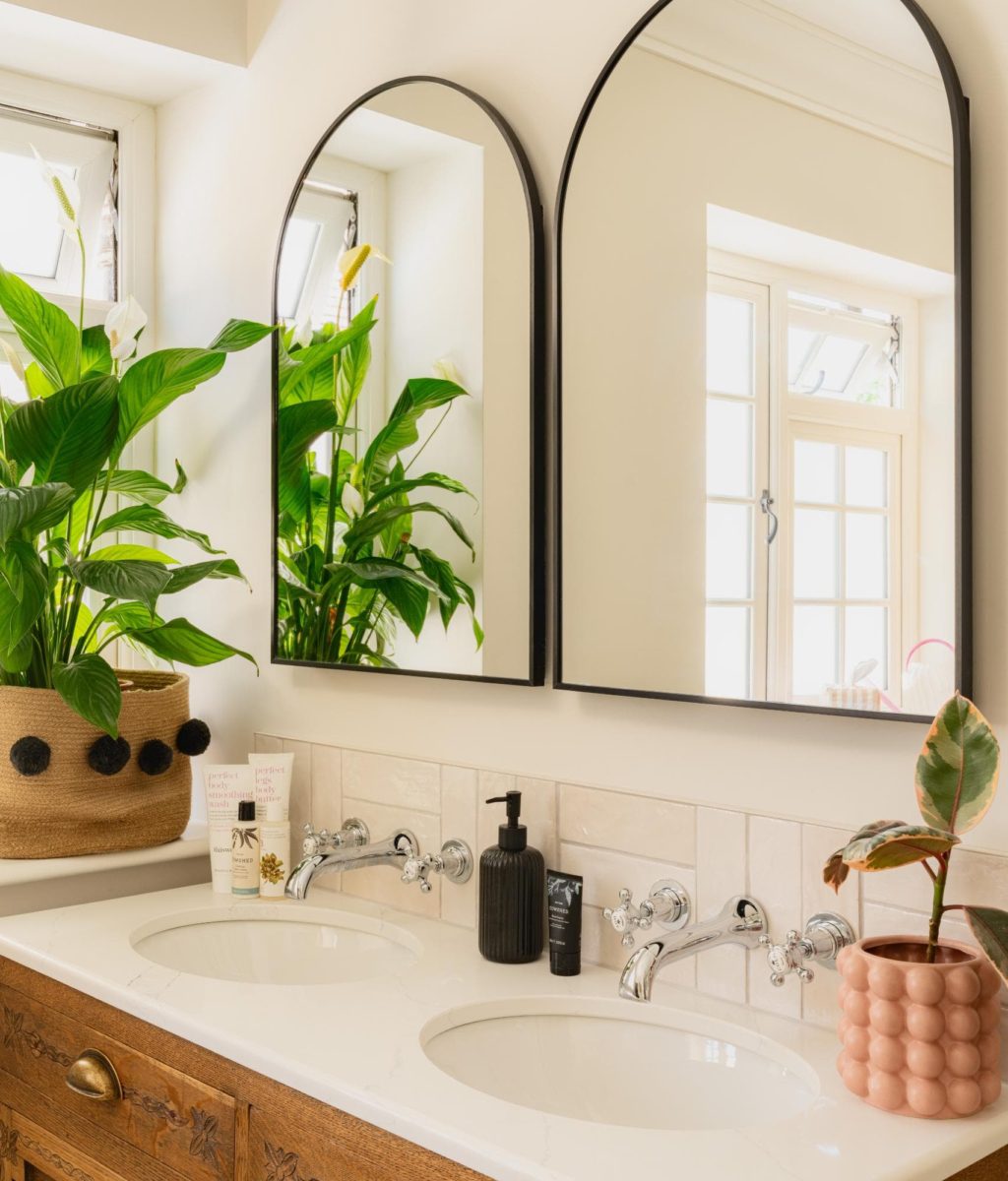 Bright contemporary bathroom with arched mirror, greenery and neutral finishes