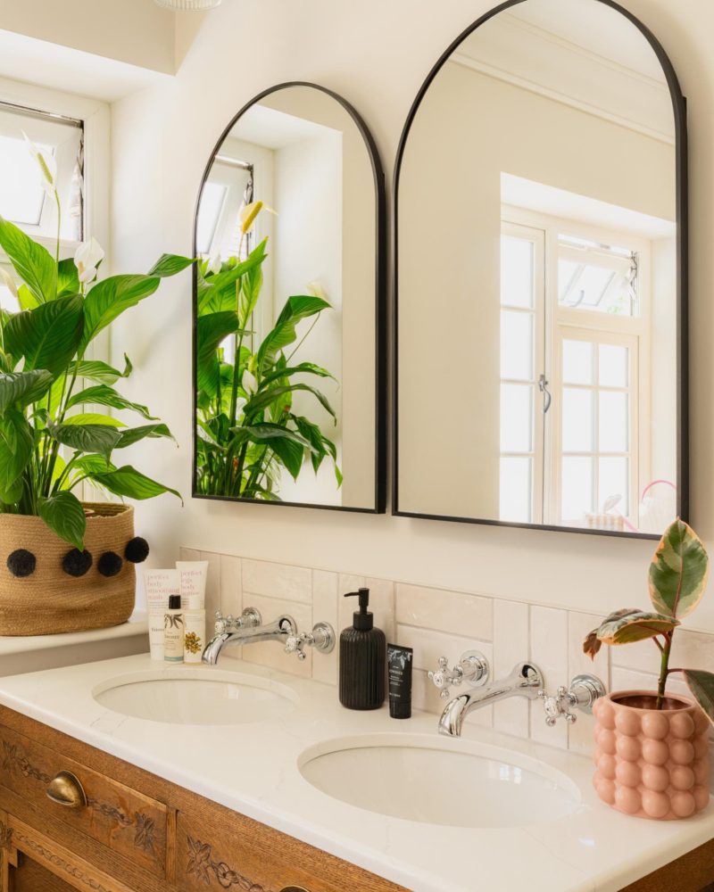 Bright contemporary bathroom with arched mirror, greenery and neutral finishes