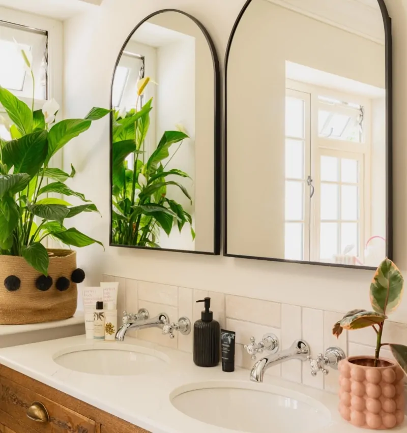 Bright contemporary bathroom with arched mirror, greenery and neutral finishes