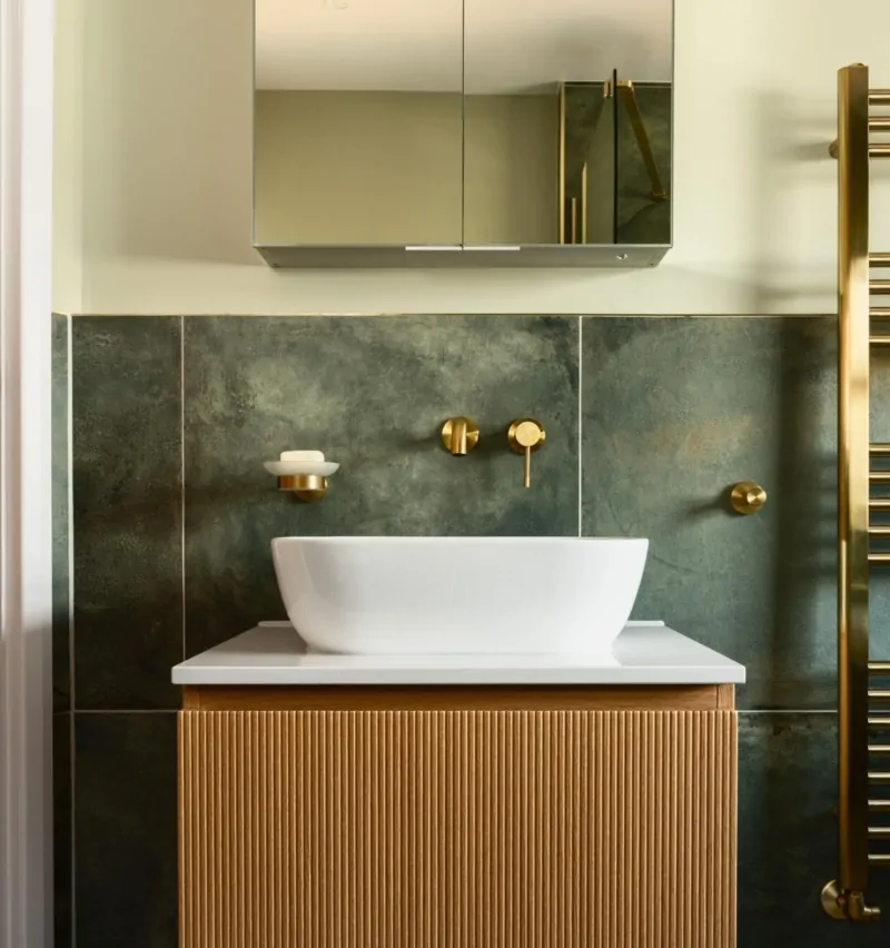 Contemporary bathroom with white vanity, green tiled wall and brass fittings