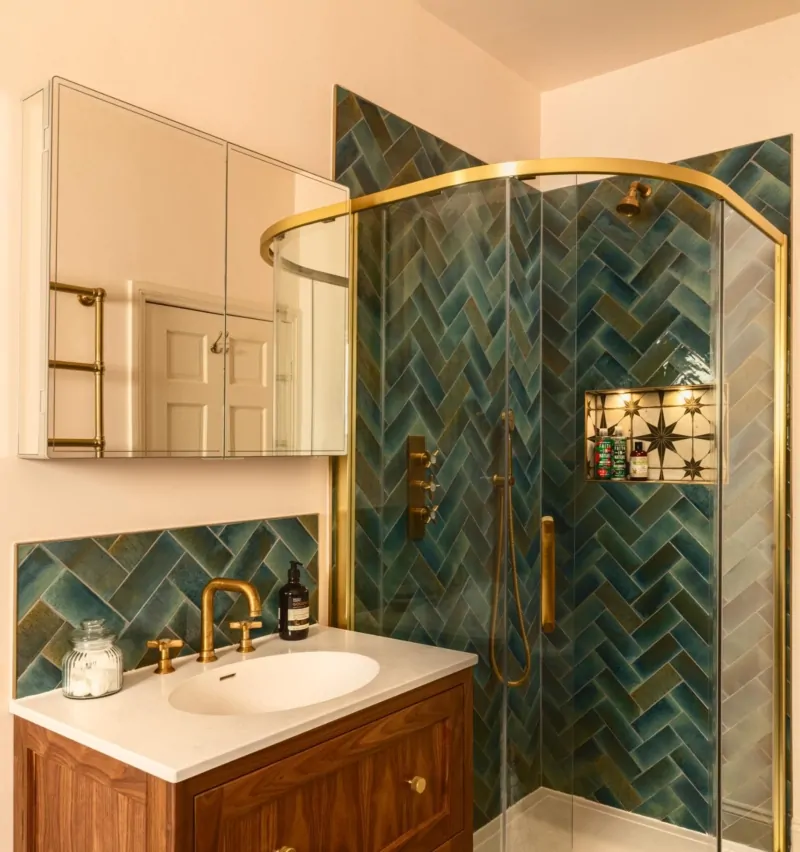 Walk-in shower with dark green herringbone tiles and brass shower frame