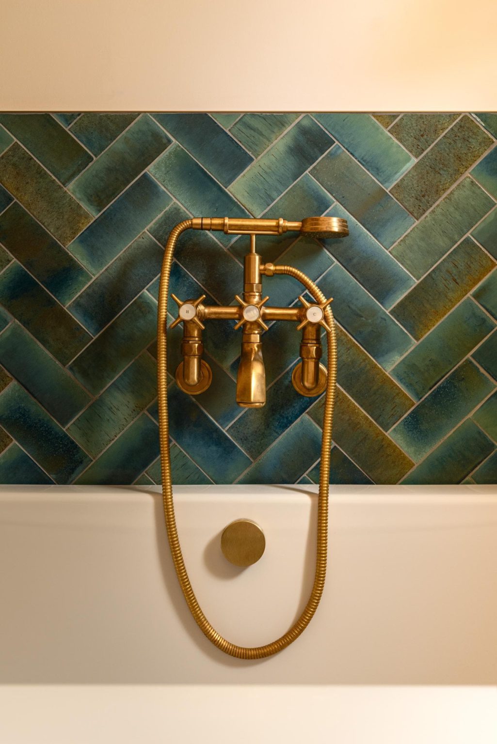 Brushed brass shower controls on dark green herringbone bathroom tiles
