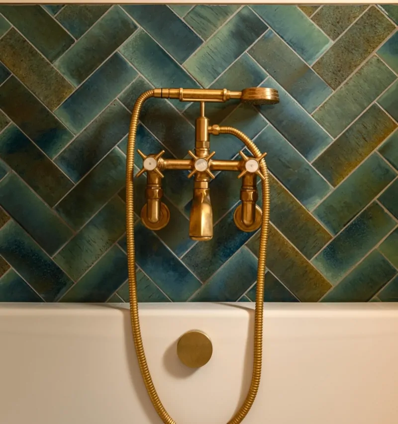 Brushed brass shower controls on dark green herringbone bathroom tiles