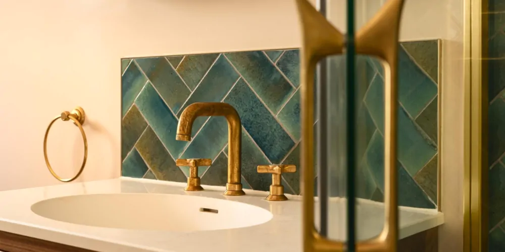 Brushed brass bathroom fitting against dark green herringbone tiles