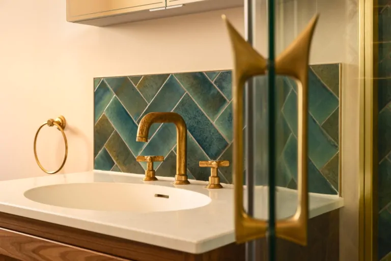 Brushed brass bathroom fitting against dark green herringbone tiles