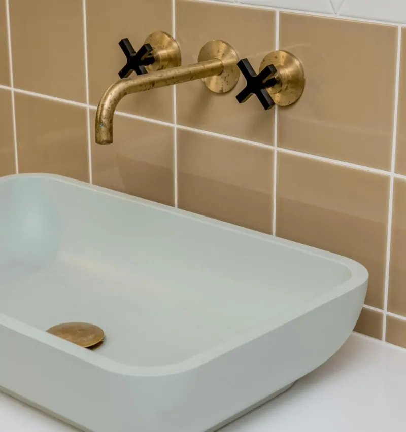 Brushed gold wall-mounted bath taps against warm beige bathroom tiles