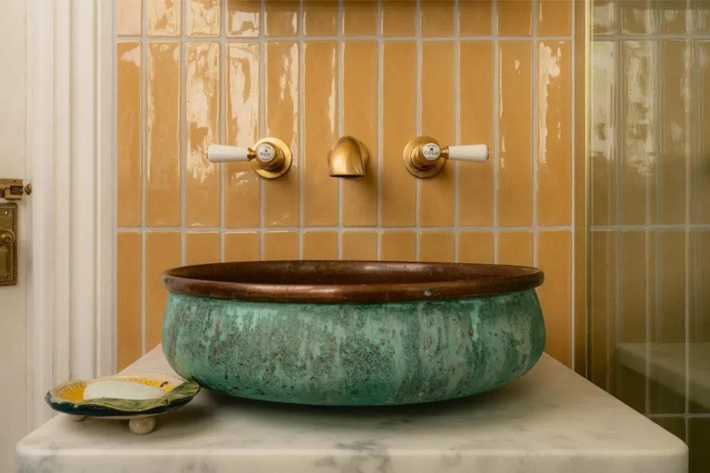 Green countertop basin with wall-mounted brass taps and vertical neutral tiles