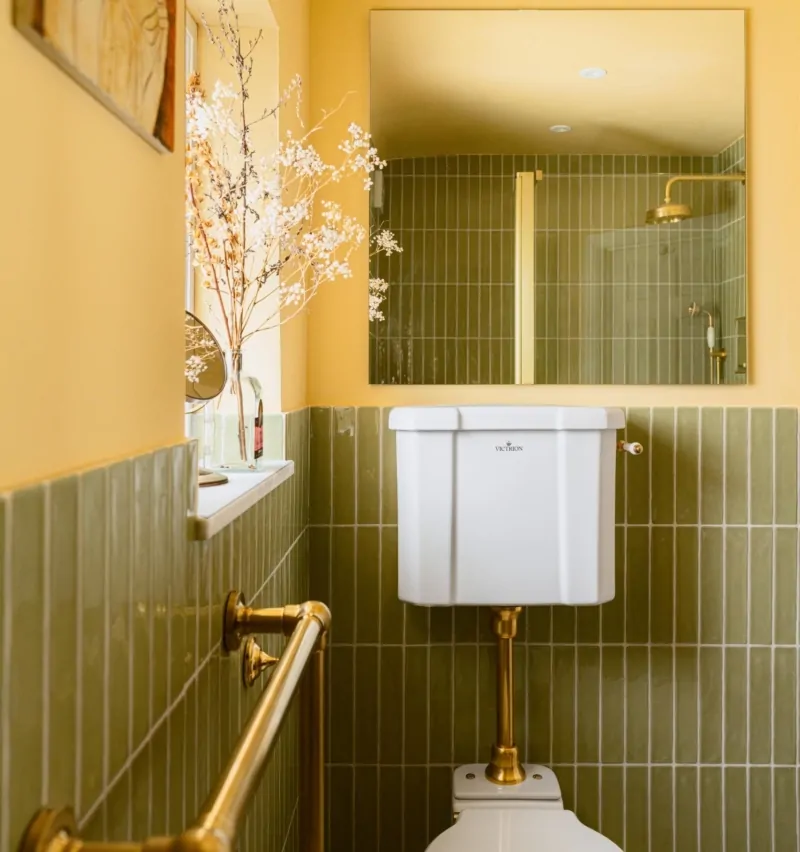 Bathroom vanity with vertical olive tiles, illuminated mirror and brass fittings