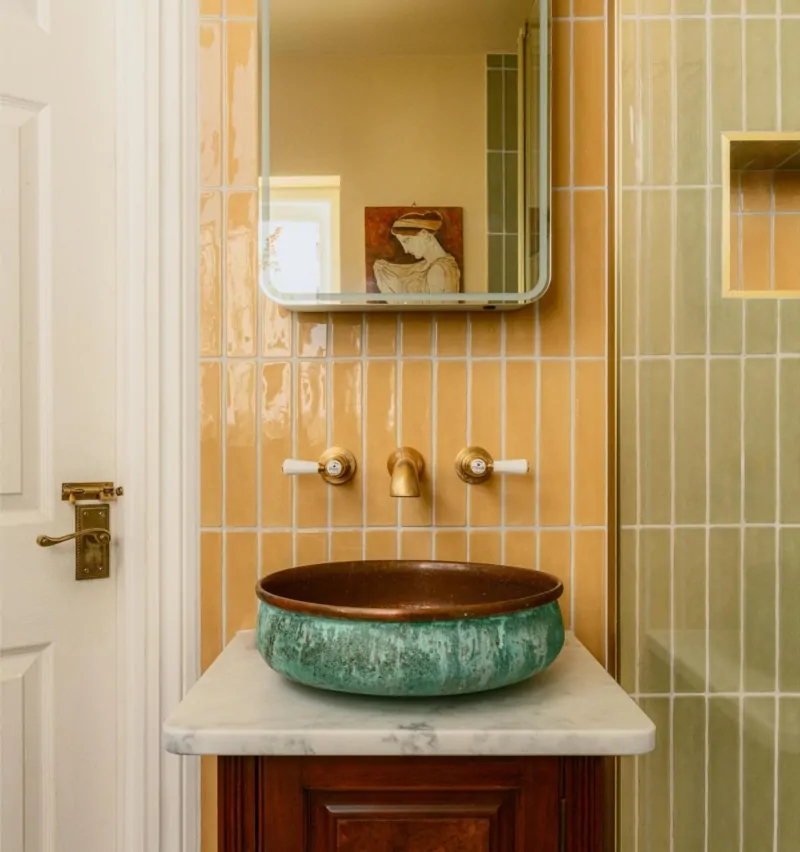 Green countertop basin with brushed brass wall-mounted taps