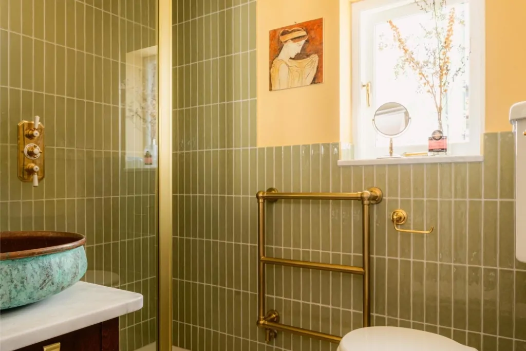 Walk-in shower with olive green vertical tiles, glass screen and brass fittings