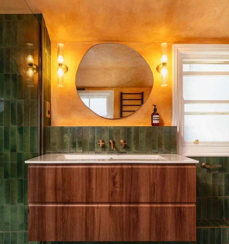 Luxury bathroom vanity with round mirror, green tiles and warm copper ceiling