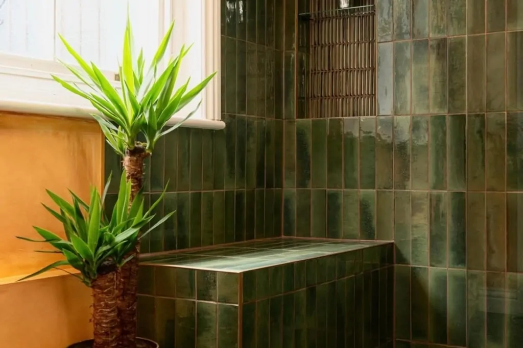 Deep green tiled bath and shower area with copper fittings and indoor plant