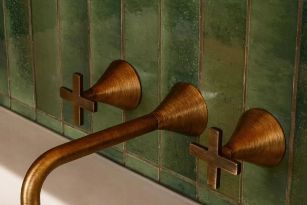 Copper wall-mounted shower controls against handmade green bathroom tiles