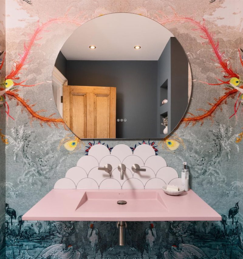 Round illuminated bathroom mirror against a dramatic artistic feature wall
