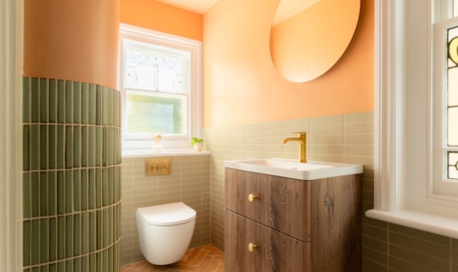 Wide view of the Clementine bathroom showing the curved green tiled partition, wall-hung toilet, wood vanity and terracotta herringbone floor.