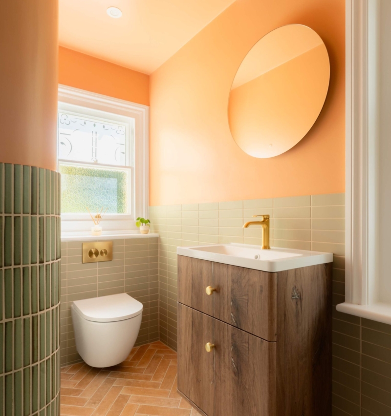 Clementine family bathroom in Hove with clementine walls, sage green tiles, terracotta herringbone flooring, wood vanity and brushed brass details.