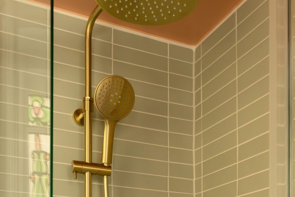 Brushed brass rainfall and handheld shower in the Clementine family bathroom in Hove, with sage green tiles and a curved shower screen.