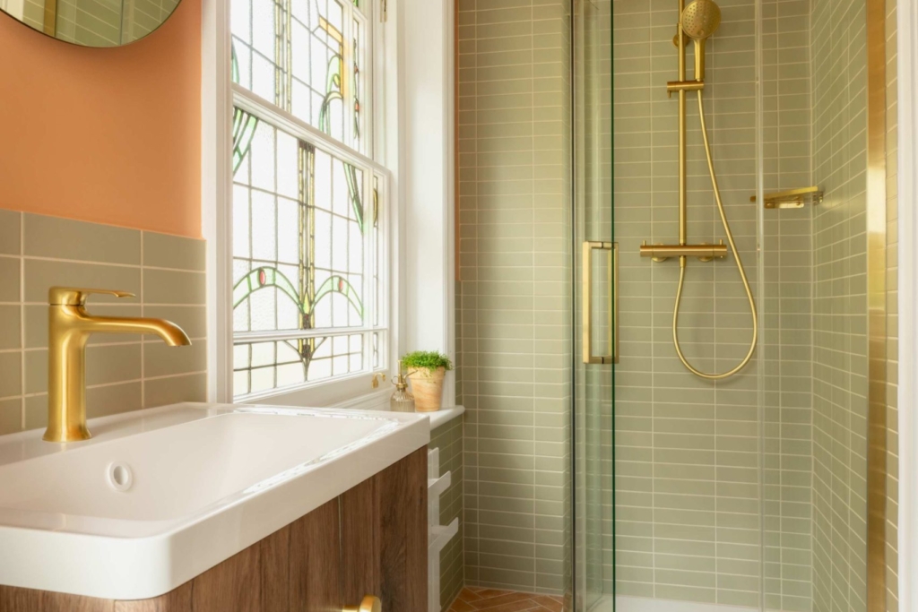 Natural wood vanity with a white basin and brushed brass tap, set against soft sage green tiles in the Clementine bathroom.