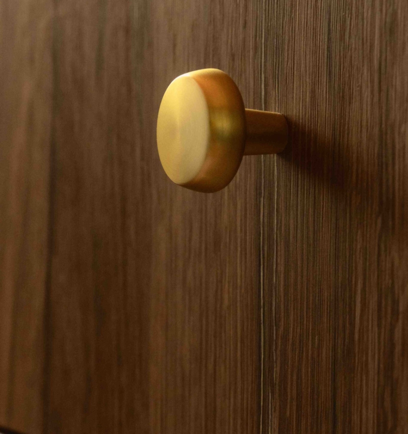 Close-up of a brushed brass round handle on the dark natural wood vanity unit in the Clementine bathroom.