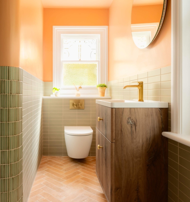 Compact family bathroom with a wood vanity, wall-hung toilet, curved tiled partition and warm clementine walls.