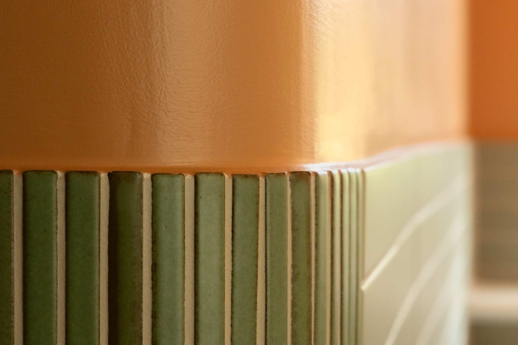 Close-up of sage green vertical tiles meeting the warm clementine wall finish in the Clementine bathroom.