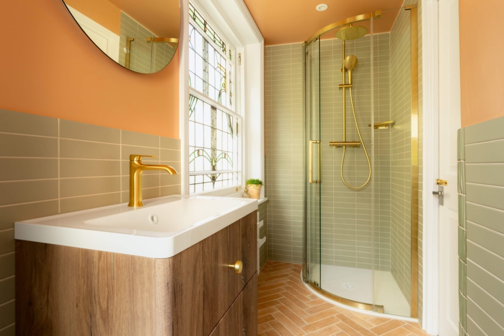 Brushed brass shower, wood vanity and terracotta herringbone floor in the warm, characterful Clementine bathroom in Hove.