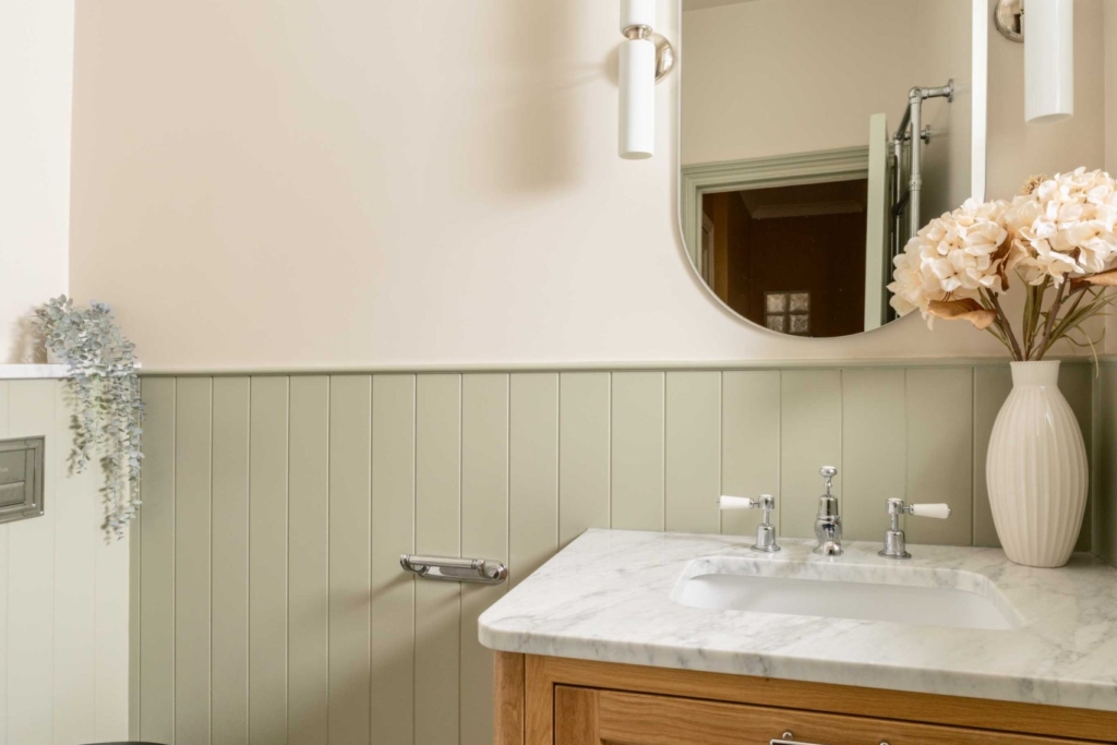 Traditional oak vanity with marble top, polished chrome taps and soft sage wall panelling in the Hampton bathroom.