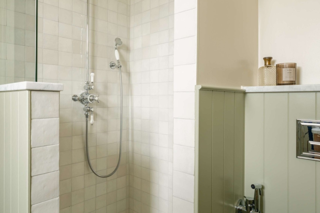 Walk-in shower with pale East Hampton marble tiles, traditional polished chrome shower fittings and basketweave mosaic flooring.
