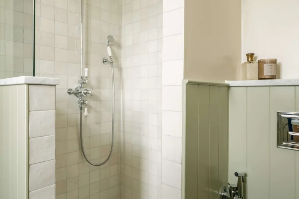 Walk-in shower with pale East Hampton marble tiles, traditional polished chrome shower fittings and basketweave mosaic flooring.