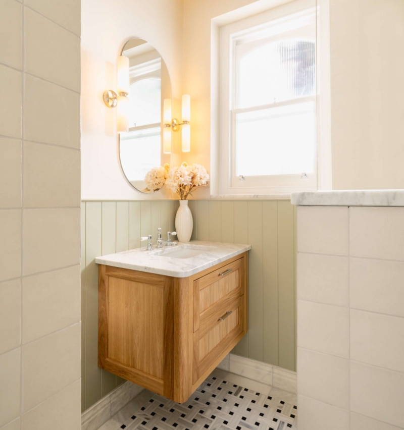 Light oak vanity with marble worktop, oval mirror and polished chrome wall lights in the Hampton bathroom.